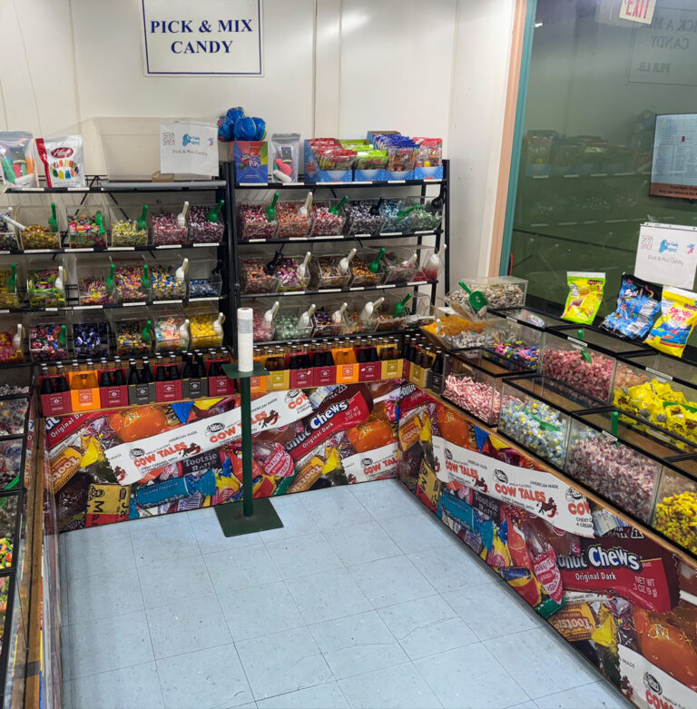 A corner of a store with many clear bins filled with candies and chocolates, and scoops for customers to pick their own candy.